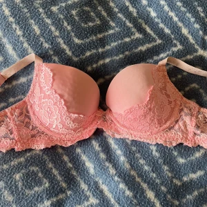 Rosa spets-bh - Söt rosa bh med detaljer i spets. Axelbanden är justerbara och bh:n har en liten metallcharm framtill.