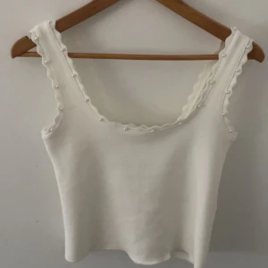 Vit ribbad linnetopp med pärlor - Supersöt vit linnetopp med ribbad struktur och croppad passform. Toppen har breda axelband med vågiga kanter och små pärlor längs hela ringningen för en extra gullig touch. Perfekt för dig som gillar stilrena detaljer och vill ha något som sticker ut. Helt ny utan prislapp