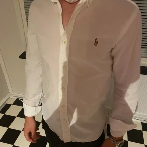 Vit skjorta från Ralph Lauren S - Klassisk vit skjorta från Ralph Lauren i slim fit-modell. Skjortan har lång ärm, knappar framtill och den ikoniska broderade loggan på bröstet. Tillverkad i bomull och passar perfekt till en clean och stilren look.