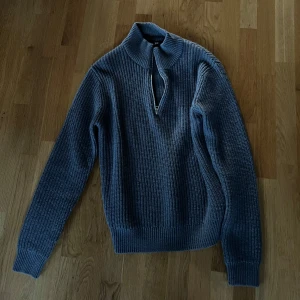 Grå stickad tröja med dragkedja - Säljer en stilren grå stickad tröja från Haglöfs. Tröjan har en praktisk dragkedja vid halsen och långa ärmar. Perfekt för kyligare dagar och ger en klassisk look.