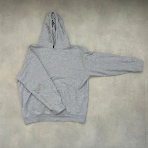 Grå hoodie - Säljer en klassisk grå hoodie med lång ärm och en praktisk ficka framtill. Perfekt för en avslappnad stil och bekväm att bära. Huvan har dragsko för justering.