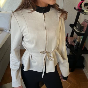 Mocka kofta - Snygg beige” jacka”med dragkedja och knytband i midjan. Jackan har en elegant peplum-design och långa ärmar. Perfekt för en stilren look.