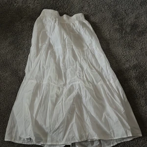 Vit långkjol från MNG - Säljer en stilren vit långkjol från MNG. Kjolen har en elastisk midja för bekväm passform och är perfekt för varma dagar. Den är tillverkad i ett lätt och luftigt material som ger en skön känsla. Perfekt för att skapa en avslappnad och chic look.