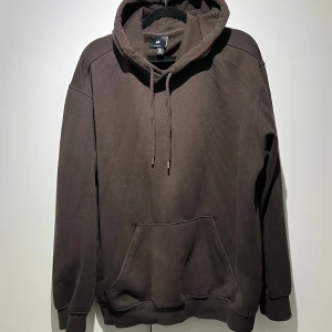 Brun hoodie från H&M - Säljer en stilren brun hoodie från H&M. Den har en klassisk design med känguruficka och justerbar huva med snören. Perfekt för en avslappnad look.
