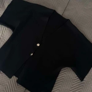 Svart kortärmad tröja med guld knappar - Snygg svart tröja med korta ärmar och guldiga knappar framtill. Perfekt för en stilren look. Passar bra till både vardag och festliga tillfällen🌺 St L men passar mig som egentligen brukar bära M & S! Aldrig använd då ärmarna är lite större än förväntat men det går att lösa! 🌺