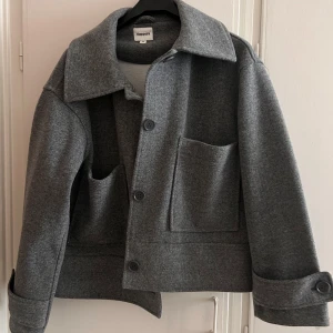 Grå ulljacka från Kappahl  - Snygg grå ulljacka från Kappahl med stora fickor och knappar framtill. Jackan har en klassisk krage och långa ärmar med knappar vid ärmsluten. Perfekt för kyligare dagar. Andvänt typ en gång nu pris 800kr