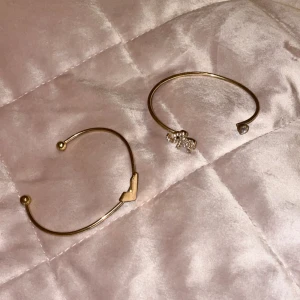 Två guldarmband med detaljer - Säljer två stilrena guldarmband. Ett armband har en V-formad detalj och det andra har en glittrig elefantsdetalj. Perfekta accessoarer för att ge din outfit en elegant touch. Inte äkta guld!  Öppen för prisförslag 