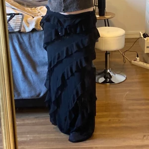 Svart långkjol från Nelly volangkjol maxokjol - Snygg svart långkjol från Nelly med volangdetaljer. Kjolen har en elegant och flytande design som ger en fin siluett. Perfekt för att skapa en stilfull look.