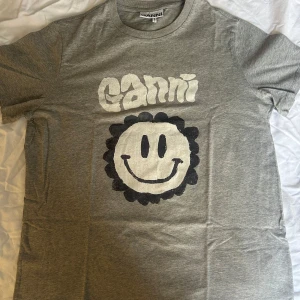 Grå t-shirt från Ganni med smiley - Säljer en grå t-shirt från Ganni med ett stort smileytryck på framsidan. T-shirten har korta ärmar och en rund halsringning. Oversized fit! Passar xs-m💞Knappt använd 