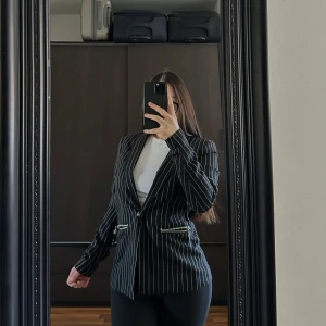 Svart randig kavaj från Rosy Boy - Snygg svart kavaj med vita ränder från Rosy Boy. Kavajen har en klassisk passform med dragkedjor vid fickorna för en modern touch. Perfekt för att ge en stilren look till din outfit.🥰🥰🥰