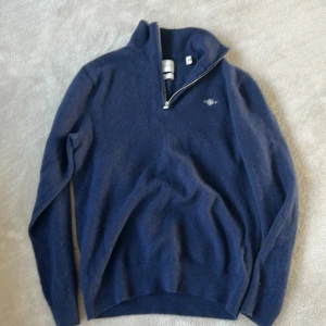 Mörkblå tröja med dragkedja - Säljer en stilren mörkblå tröja med halv dragkedja och hög krage. Tröjan har långa ärmar och en liten logga på bröstet. Perfekt för kyligare dagar.Den har krymp lite men är en Medium men upplevelse som Smal