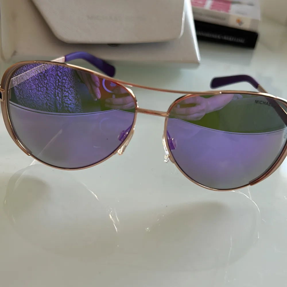 Snygga solglasögon från Michael Kors med lila spegelglas och guldfärgad metallram. De har en klassisk pilotform som ger en tidlös look. Perfekta för soliga dagar och kommer med ett stilrent fodral.. Asusteet.