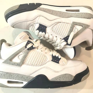 Nike Air Jordan 4 Retro - Säljer ett par Nike Air Jordan 4 Retro i vit och grå med mörkblåa och röda detaljer. Skorna har en klassisk design med snörning och en robust sula. Perfekta för sneaker-entusiaster! Skickas inom 24 timmar och pris kan alltid diskuteras 