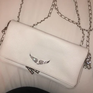 Vit axelväska med kedja - Snygg vit axelväska med kedja och dekorativt emblem framtill. Äkta läder