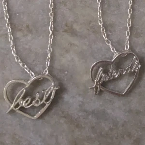 Silverfärgade best friends-halsband - Två matchande silverfärgade halsband med hjärtformade hängen. Ena hänget har texten 'best' och det andra 'friends'. Perfekta för att dela med din bästa vän! 💖