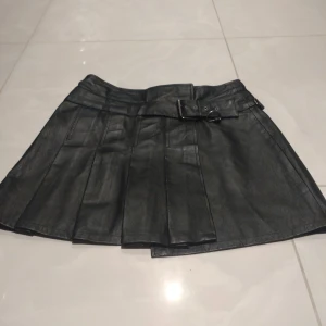 Svart skinnkjol från F & Co - Snygg svart skinnkjol från F & Co med bälte och veckade detaljer. med kardborre fäste. Köpt på Humana.