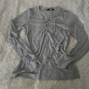 Grå långärmad tröja från BikBok - Säljer en stilren grå långärmad tröja från BikBok med snörning framtill. Perfekt för en avslappnad look. Tröjan har en mjuk och bekväm passform. Det står att storleken är M men är som s men jag har storlek xs och använde den