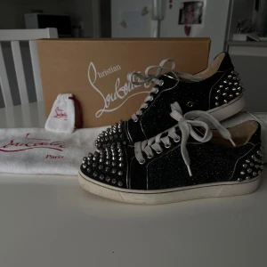 Christian Louboutin, svart-glittriga  - Hej! ❤️Säljer mina snygga svarta sneakers från Christian Louboutin då jag inte använder dom längre. Dom har en glittrig yta som gör dom riktigt stiliga och även nitar fram och bak. Dom är köpta i Italien, storlek 36. Väldigt fina skor med lite defekter: vissa spikar har tappat lite färg, men ingenting som märks när man har på sig dom & skosnöret på höger sko är lite trasigt, men ingenting som inte går att fixa. Annars är dom i bra skick! Tveka inte på att fråga om du undrar något 💌