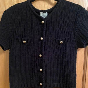 Svart kortärmad kofta med guldknappar - Säljer denna top då den endast kommit till användning 1 gång. Köpt för ca 399kr och säljes för 150kr. Endast seriösa köpare tack☺️