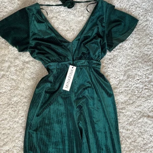 Grön jumpsuit från MINKPINK - Snygg grön jumpsuit från MINKPINK med v-ringning och korta ärmar. Den har en elegant knytning i ryggen och vida ben. Perfekt för en stilfull look.