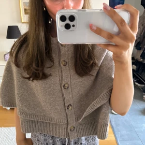 Beige kofta med knappar - Säljer en stilren beige kofta med knappar framtill. Den har en lös passform och ribbade kanter som ger en snygg detalj. Perfekt för lager-på-lager-stil.