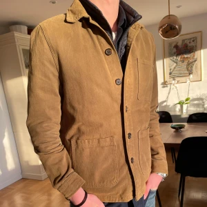 Brun/grön  jacka med knappar - Snygg grön/brun jacka med knappar framtill och två stora fickor. Perfekt för höst och vår. Jackan har en klassisk krage och långa ärmar.