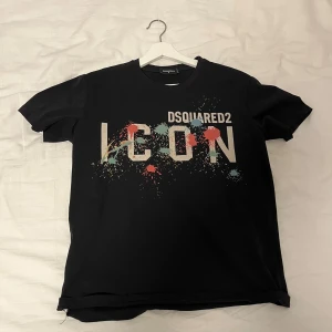 Svart t-shirt från Dsquared2 - Snygg svart t-shirt från Dsquared2 med stort 'ICON' tryck i färgglada stänk på framsidan. Perfekt för en cool och avslappnad stil. Tillverkad i Italien. Pris sänks vid snabbaffär.