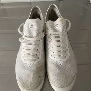 Vita fotbollsskor från Umbro - Säljer ett par vita fotbollsskor från Umbro med snörning och rund tå. Skorna har en diskret grå detalj på sidan och är perfekta för fotbollsträning eller match.