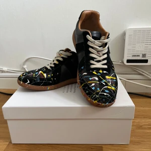 Svarta sneakers med färgstänk - Unika svarta sneakers med coola färgstänk i gult, blått och vitt. Skorna har en rund tå och snörning, vilket ger en bekväm passform. Perfekta för att ge din outfit en konstnärlig touch.