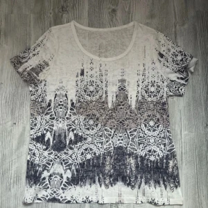 Vit och svart mönstrad t-shirt Medium - Säljer en snygg see-through vit t-shirt med ett unikt svart mönster som ger en cool effekt. T-shirten har korta ärmar och en rund halsringning.  Tvättlappen avklippt och där har det blivit ett litet hål