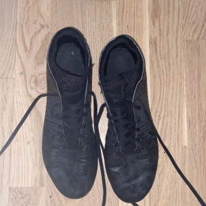 Svarta fotbollsskor med snörning - Säljer ett par svarta fotbollsskor med snörning och rund tå. Skorna har en mönstrad yta och dobbar för bra grepp på planen. Perfekta för fotbollsträning eller match.