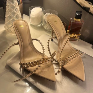 Beige klackskor med guldiga nitar från Zara - (Intressekoll) Snygga beige klackskor från Zara med spetsig tå och guldiga nitar.  Jättesnygg och trendiga!! Helt oanvända dessutom. Ca 8-10 cm klack 🩷🩷