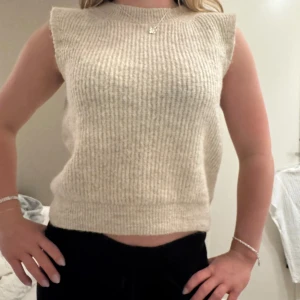 Beige ribbad ärmlös topp - Säljer en stilren beige ribbad topp med ärmlös design. Perfekt för lager-på-lager eller som den är. Enkel och snygg för alla tillfällen.