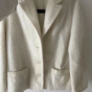 Vit kappa - Elegant vit kappa med en klassisk design. Den har långa ärmar och knappar framtill. En knapp har gått av men lätt att sy på eller om man vill klippa bort någon annan knapp💗Den har ingen storlek men jag skulle uppskatta den till en S. Färgen är krämvit!