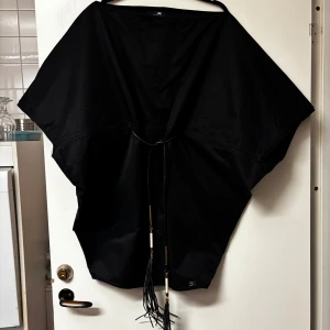 Svart kaftan från Elisabetta Franchi - Elegant svart kaftan från Elisabetta Franchi med löst passform och dekorativa snören framtill. Perfekt för en stilren look.