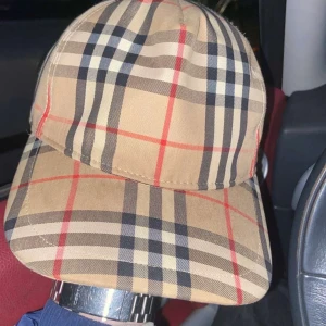  keps från Burberry - Snygg rutig keps från Burberry i klassiskt beige, svart och rött mönster. Kepsen har en justerbar rem baktill och en broderad logotyp på sidan. Säljer den då den inte används mer och är i ett extremt bra skick och såklart är den äkta. Vid frågor är det bara att skicka eyy medelande😊