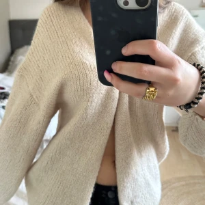 Beige stickad kofta - Mysig beige stickad kofta med en avslappnad passform. Perfekt för kyliga dagar och ger en stilren look. Koftan har en öppen design och långa ärmar.