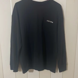 Svart långärmad tröja med text - Säljer en svart långärmad tröja med texten 'EYES OPEN' tryckt på bröstet. Enkel och stilren design som passar till det mesta. Perfekt för en avslappnad look.