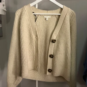 Beige ribbad kofta - Säljer en beige kofta med ribbad struktur och stora knappar framtill. Koftan har en v-ringad design och långa ärmar, perfekt för kyligare dagar. Den är både mysig och trendig! Använd fåtal gånger men kommer inte till användning längre🩷