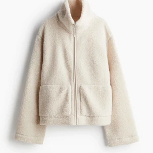Beige teddyjacka med dragkedja - Mysig beige teddyjacka med dragkedja och hög krage. Perfekt för kyliga dagar med sina stora fickor och mjuka material.