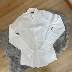 Vit skjorta från Tiger of Sweden - Säljer en stilren vit skjorta från Tiger of Sweden i extra slim passform. Skjortan har långa ärmar och klassisk krage med knappar framtill. Perfekt för en elegant look.