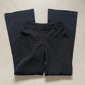 Svarta randiga kostymbyxor från H&M - Snygga svarta kostymbyxor från H&M med diskreta ränder. Byxorna har en klassisk passform med raka ben och hällor för bälte. Perfekta för en stilren look.