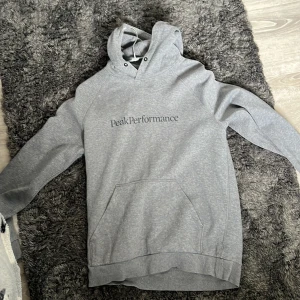 Grå hoodie från Peak Performance - Säljer en stilren grå hoodie från Peak Performance. Tröjan har en klassisk design med en känguruficka framtill och en justerbar huva. Perfekt för en avslappnad look. 🩶