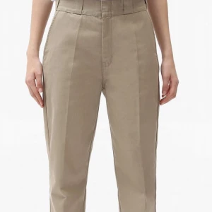 Beige byxor från Dickies - Snygga beige byxor från Dickies med hög midja och klassisk design. Byxorna har en rak passform och är tillverkade i slitstarkt material. Perfekta för en stilren look.