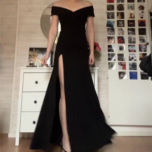 Svart balklänning med slits - Elegant svart långklänning med offshoulder-design och en djärv slits framtill. Klänningen har en omlott-detalj som ger en smickrande passform. Perfekt till bal eller en speciell tillställning. Endast testad, aldrig använd. Storlek xs, ifrån bubbelroom. Köpt för 900kr i januari.