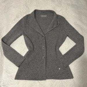 Grå cardigan  - Snygg grå cardigankavaj med knappar framtill. Den har en elegant krage och långa ärmar, perfekt för en stilren look. Passar bra till både vardag och mer uppklädda tillfällen.