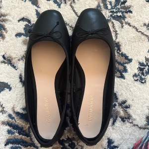 Svarta ballerinaskor från Primark - Säljer ett par klassiska svarta ballerinaskor från Primark. De har en söt rosett på ovansidan och en rund tå. Perfekta för en stilren look.