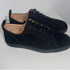 Svarta sneakers från Christian Louboutin - Snygga svarta sneakers i mocka från Christian Louboutin med den ikoniska röda sulan. Skorna har snörning och en rund tå, vilket ger en stilren look. Perfekta för dig som vill ha en touch av lyx i vardagen.