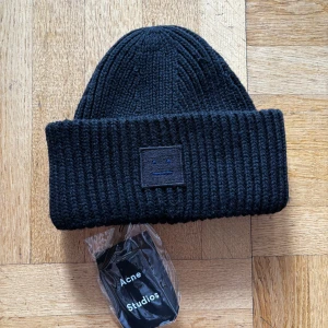 Svart stickad mössa från Acne Studios - Snygg svart stickad mössa från Acne Studios med ribbad design och en diskret logotyp framtill. Perfekt för att hålla värmen under kyliga dagar. Mössan är i one size och passar de flesta huvudstorlekar. Färg: Svart