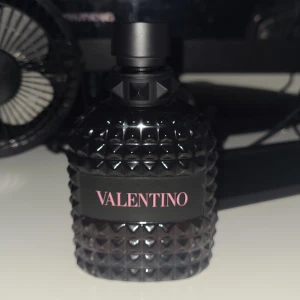 Svart parfymflaska från Valentino 75ml tror jag  - Elegant svart parfymflaska från Valentino med ett unikt nitat mönster. Flaskan har en stilren design med en svart kork och en tydlig logotyp på framsidan. Perfekt för den som vill ha en lyxig och modern doftupplevelse. Har dock använt den 